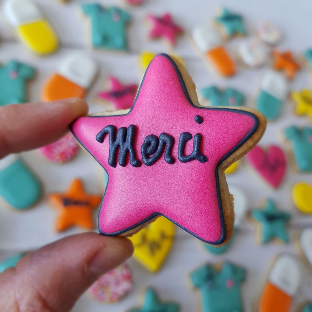 pink star cookie with the word merci written on it extra royal icing for storing